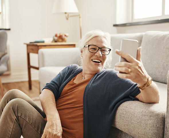 older woman using her cell phone sitting by the couch