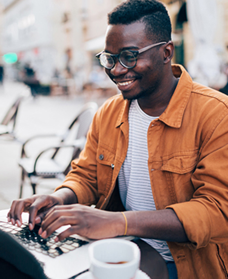 Un jeune homme souriant, travaillant sur un ordinateur portatif à l’extérieur