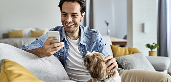Happy man texting on mobile phone while relaxing with his dog at home