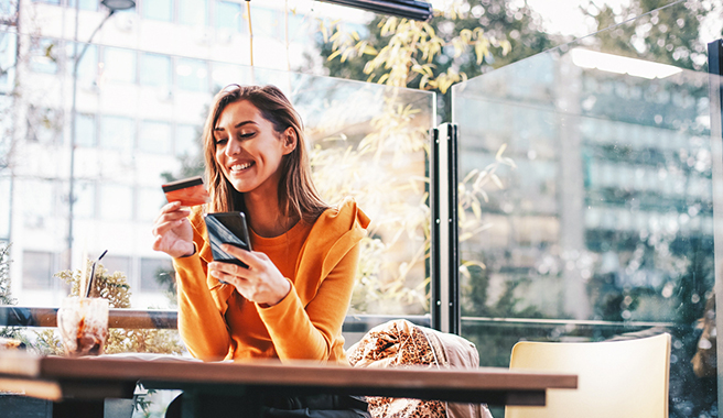 Une femme tenant son téléphone et sa carte de débit dans un café