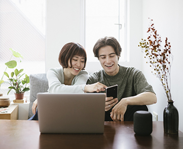 Un jeune couple assis et souriant à un bureau en regardant un ordinateur portatif