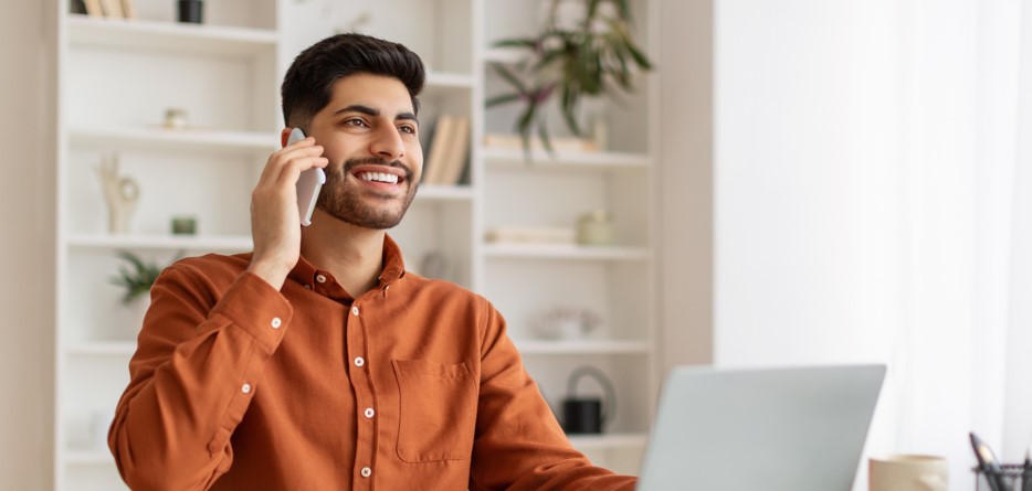 Jeune homme souriant parlant au téléphone à la maison