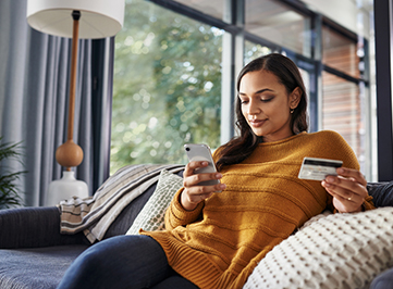 woman using her phone and debit card on the couch